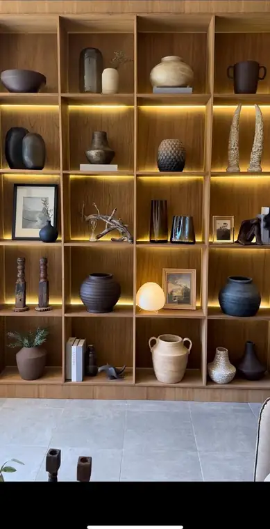 Biblioteca de madera con luz cálida, ánforas, cuencos y esculturas de cerámica Lumox Decor